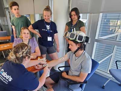Students gathered around a man wearing an electronic device on his head.