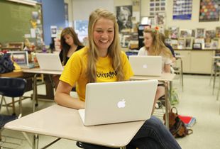 High school student sitting at her desk laughing.